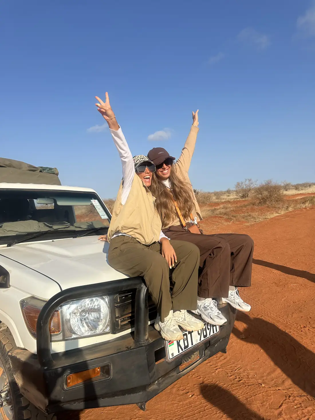 Due viaggiatrici sedute sul cofano della jeep in safari